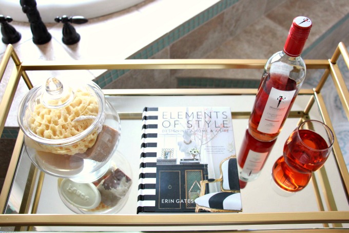 A book, wine, and bath beads are great essentials for a bathroom bar cart. www.jennelyinteriors.com
